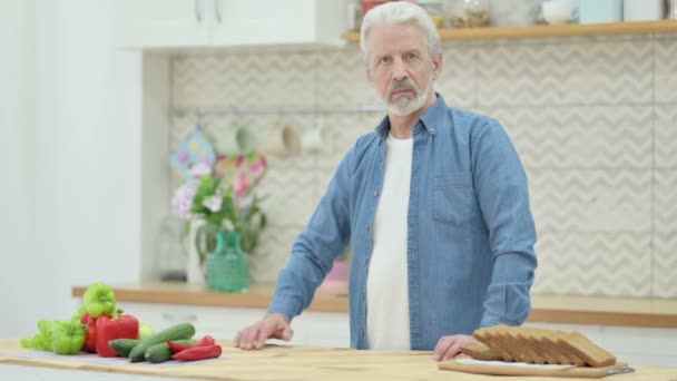 Здоровый пожилой человек показывает большие пальцы вниз, стоя на кухне — стоковое видео
