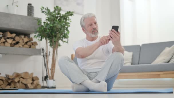 Старша людина використовує смартфон на Yoga Mat вдома — стокове відео