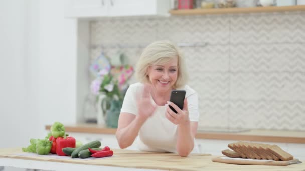 キッチンでスマートフォンでビデオ通話を行う魅力的なシニア老婦人 — ストック動画