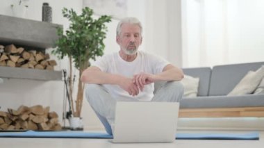 Yaşlı adam videoda konuşuyor. Evde Yoga Mat 'e telefon var.