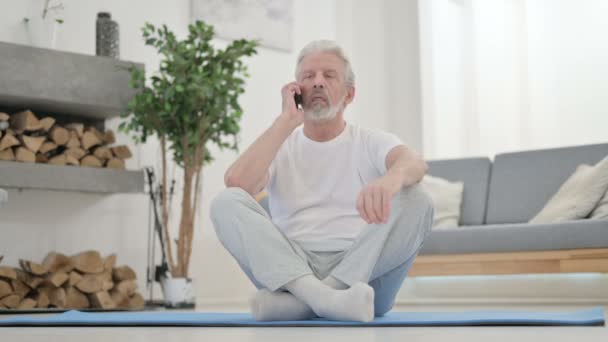 Senior Old Man talar på smartphone på Yogamattan hemma — Stockvideo
