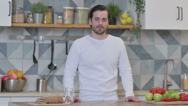 Młody człowiek pokazuje kciuki w dół stojąc w kuchni — Wideo stockowe