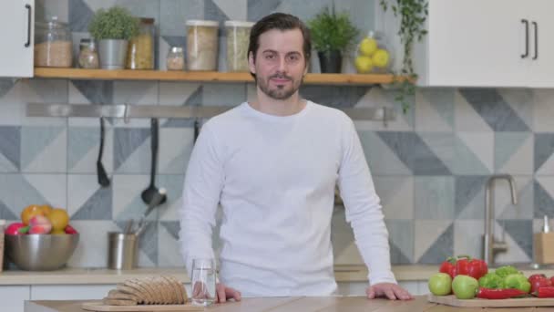 Молодий чоловік посміхається в камеру стоячи на кухні — стокове відео