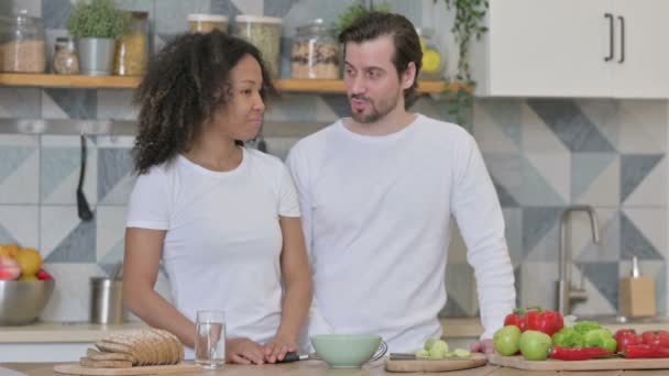 Seria mixta carrera pareja hablando mientras de pie en cocina — Vídeo de stock