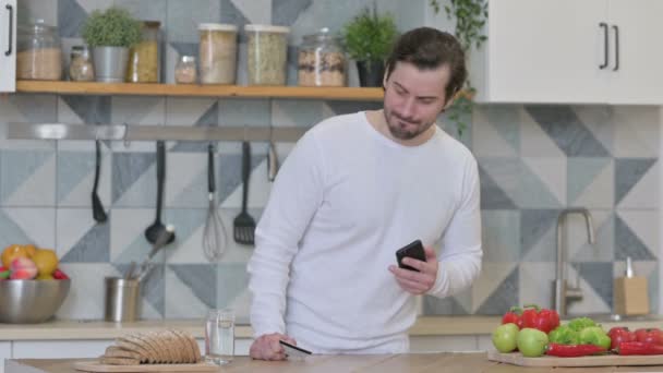 Unge man gör online betalning på smartphone i köket — Stockvideo