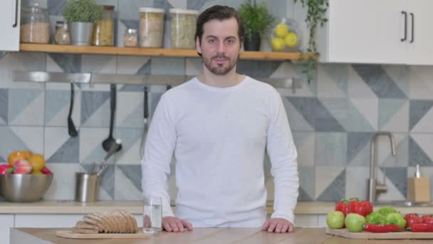 Jeune homme regardant la caméra alors qu'il se tenait dans la cuisine — Video