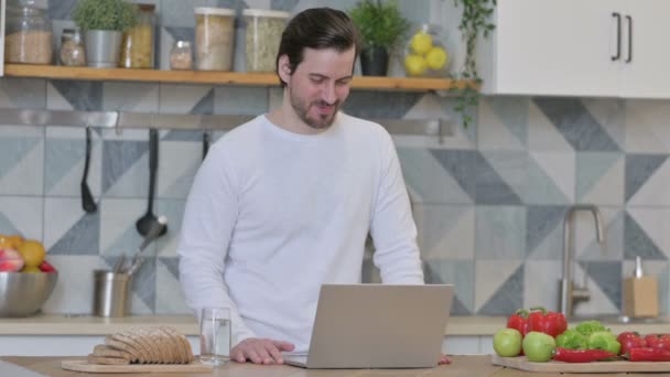 Ung man gör video samtal på laptop i köket — Stockvideo