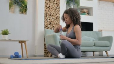 Evde yoga yaparken su içen yorgun Afrikalı kadın.