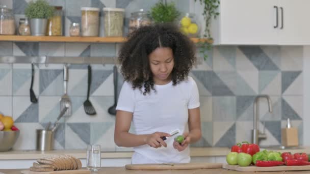 Attrayant jeune femme africaine épluchage concombre dans la cuisine — Video