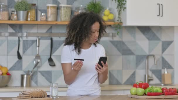 台所でスマートフォンでオンライン決済を行うアフリカの女性 — ストック動画