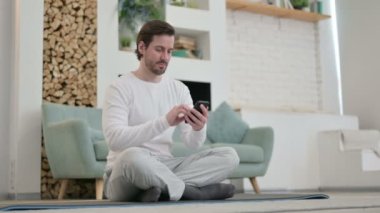 Evde Yoga Mat 'te akıllı telefon kullanan genç adam.