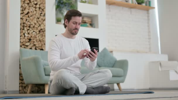 Молодий чоловік користується смартфоном на Йога Мат вдома. — стокове відео