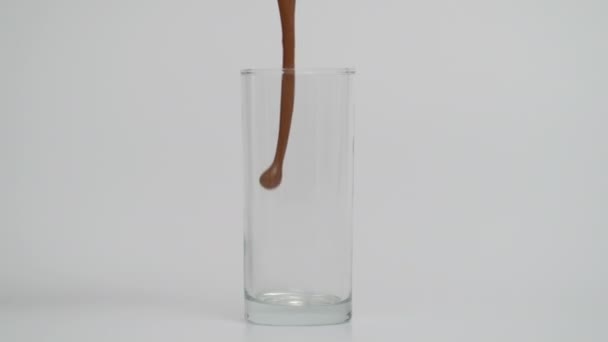 Mouvement super lent de verser du lait au chocolat dans du verre transparent, fond bleu — Video