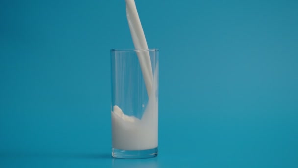 Movimento lento de derramamento de leite em vidro a 1000 fps, fundo azul — Vídeo de Stock