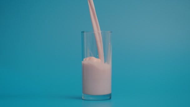 Super pomalý pohyb nalévání mléka ve skle, modré pozadí — Stock video