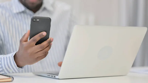 Primo piano di uomo africano utilizzando smartphone e laptop — Foto Stock