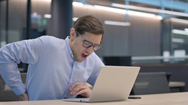 Dizüstü bilgisayarı olan genç adam sırt ağrısı çekiyor.