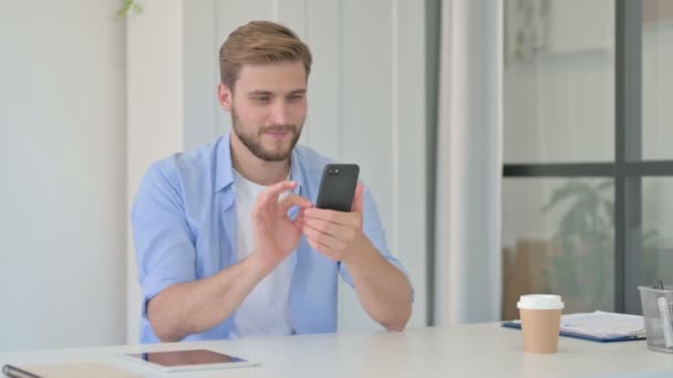 Young Creative Man viert succes op Smartphone in Office — Stockvideo