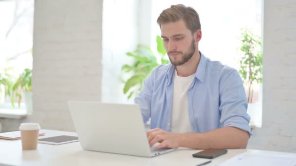 Joven hombre creativo con el ordenador portátil sonriendo en la cámara — Vídeos de Stock