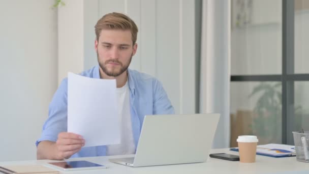 Δημιουργικός άνθρωπος με laptop ανάγνωση εγγράφων στο γραφείο — Αρχείο Βίντεο