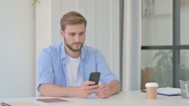 Ofiste akıllı telefon kullanan çekici genç yaratıcı adam. 