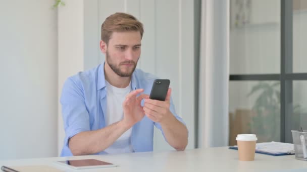 Joven hombre creativo reaccionando a la pérdida en el Smartphone en la oficina — Vídeo de stock