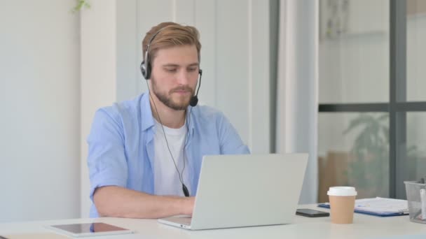 Δημιουργικός άντρας που μιλάει σε ακουστικά, εργάζεται σε φορητό υπολογιστή στο γραφείο — Αρχείο Βίντεο