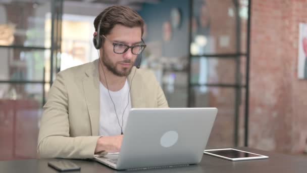 Человек в наушниках работает над ноутбуком на работе — стоковое видео