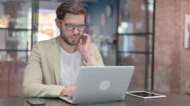 Dizüstü bilgisayarı olan genç adam iş yerinde boyun ağrısı çekiyor. 