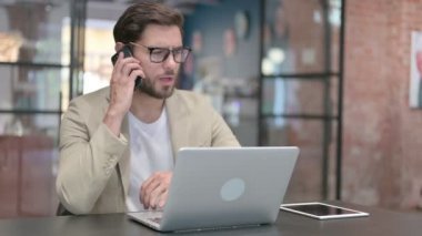 Dizüstü bilgisayarlı genç adam Smartphone 'da konuşuyor 