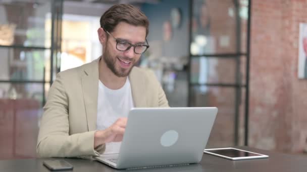 Молодий чоловік розмовляє на відео дзвінок на ноутбук на роботі — стокове відео
