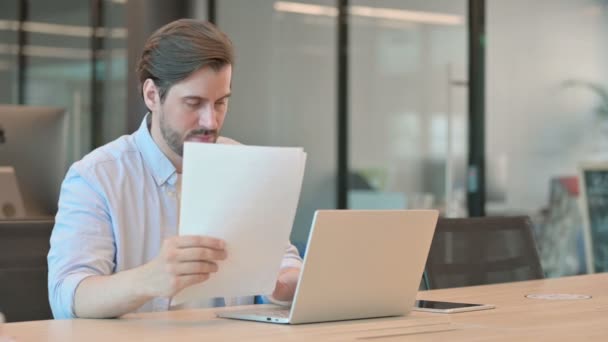 Зрілий дорослий чоловік з ноутбуком читання документів в офісі — стокове відео