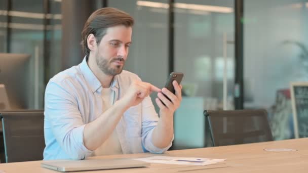 Reifer erwachsener Mann feiert Erfolg mit Smartphone im Büro — Stockvideo