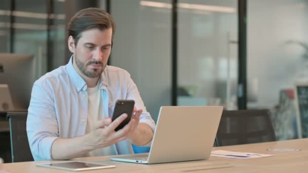 Ofiste akıllı telefon kullanan dizüstü bilgisayarlı olgun yetişkin adam — Stok video