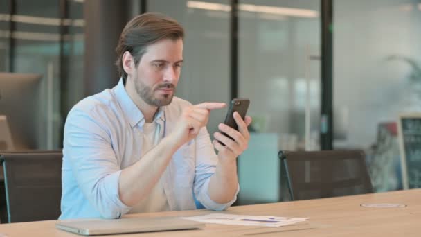 Reifer erwachsener Mann reagiert auf Verlust mit Smartphone im Büro — Stockvideo