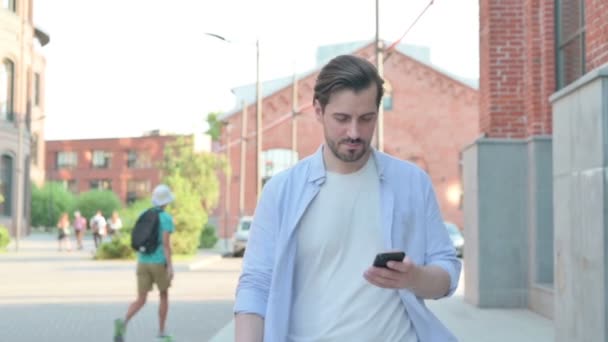 Mann feiert mit Smartphone, während er in Zeitlupe auf der Straße läuft — Stockvideo