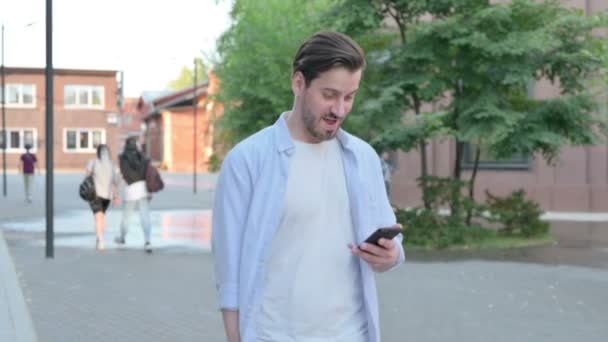 Mann feiert Erfolg am Telefon, während er auf der Straße läuft — Stockvideo
