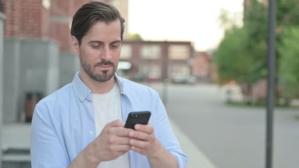 Человек, использующий смартфон, стоя на улице — стоковое видео