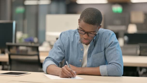 Hardwerkende jonge Afro-Amerikaanse man schrijft op papier in kantoor — Stockvideo