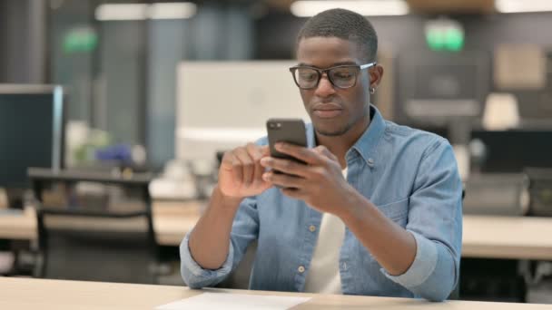Привлекательный молодой афроамериканец с помощью смартфона в офисе — стоковое видео