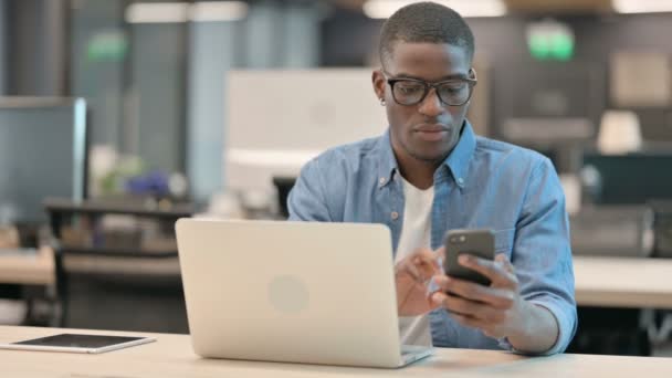Un tânăr afro-american folosește smartphone-ul la locul de muncă — Videoclip de stoc