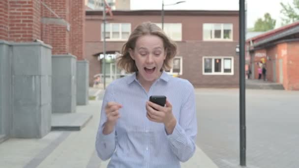 Женщина празднует успех на смартфоне во время прогулки по улице — стоковое видео