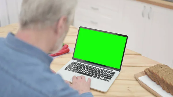 Viejo usando el ordenador portátil con la pantalla dominante del croma en la cocina — Foto de Stock