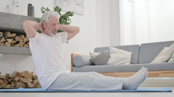 Velho fazendo alongamentos em esteira excercise em casa — Fotografia de Stock