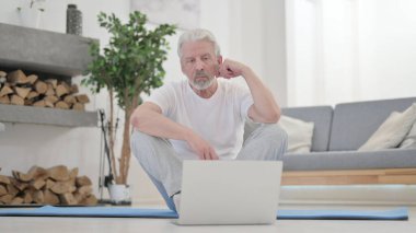 Yaşlı adam evde egzersiz yaparken dizüstü bilgisayar kullanıyor.