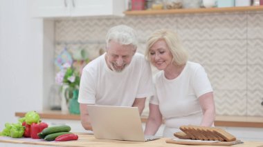 Mutfakta dizüstü bilgisayarda çalışan yaşlı çift.