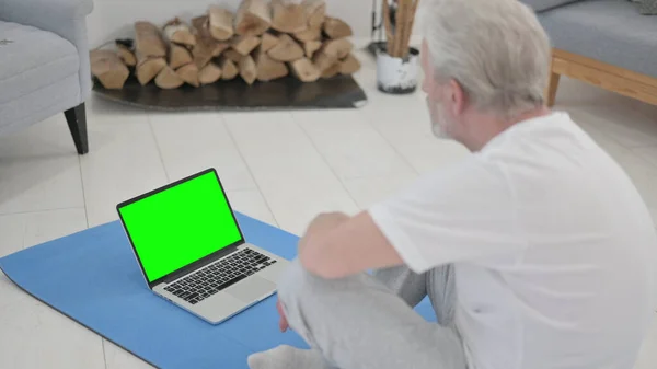 Cvičení starý muž pomocí notebooku se zelenou obrazovkou na Jóga Mat — Stock fotografie