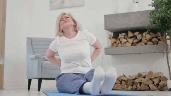 Gammal kvinna som har ont i ryggen när hon gör yoga hemma — Stockfoto