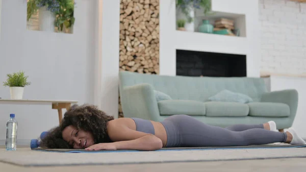 Уставшая африканская женщина лежит дома на коврике для упражнений — стоковое фото