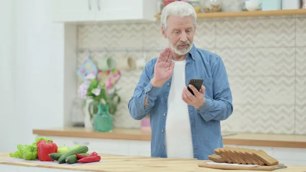 Vieil homme faire appel vidéo sur Smartphone tandis que debout dans la cuisine — Photo